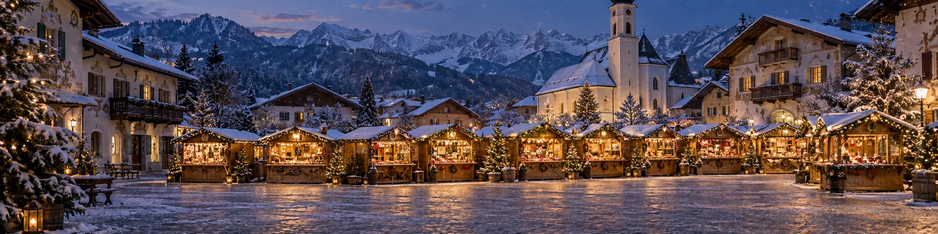 Christkindlmarkt vor Häusern mit bemalten Fassaden und einer Zwiebelturmkirche, dahinter die Alpenkette