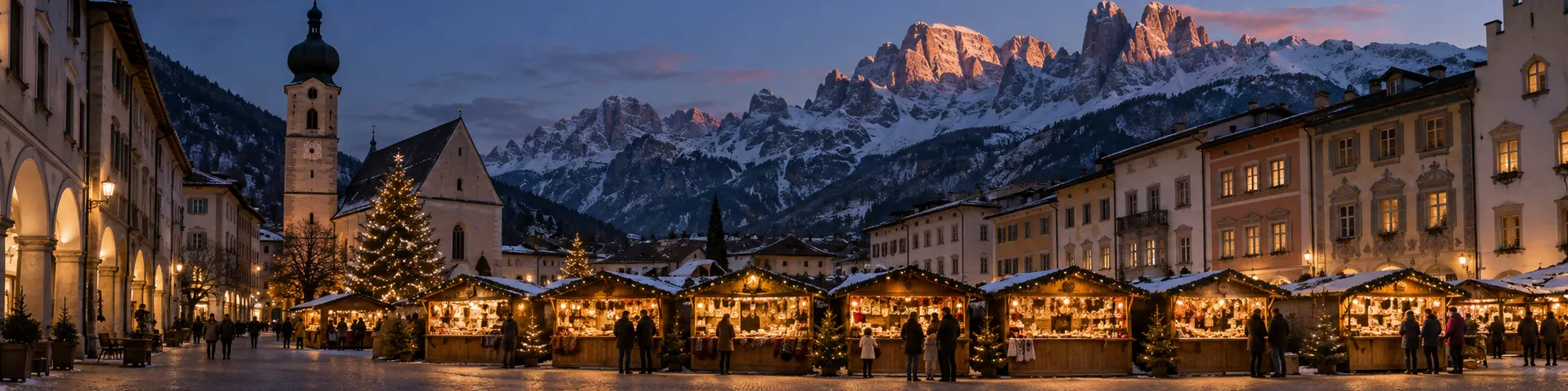 Christkindlmarkt mit beleuchteten Holzhütten vor verschneiten Felsgipfeln